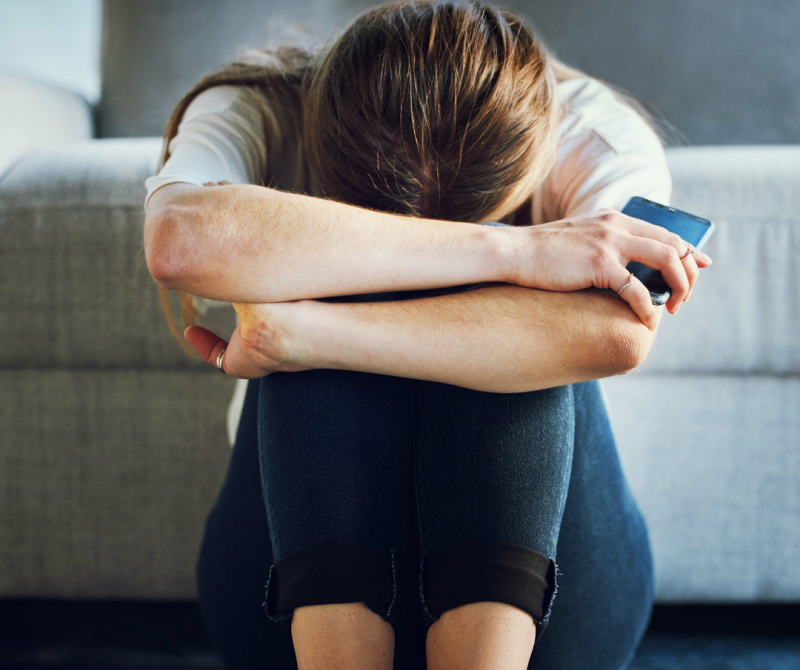 There is help to reduce stress and anxiety naturally. Woman sitting on the floor with head resting on knees, overwhelmed by chronic pain and dizziness that may be alleviated through upper cervical care for neck and back pain relief.