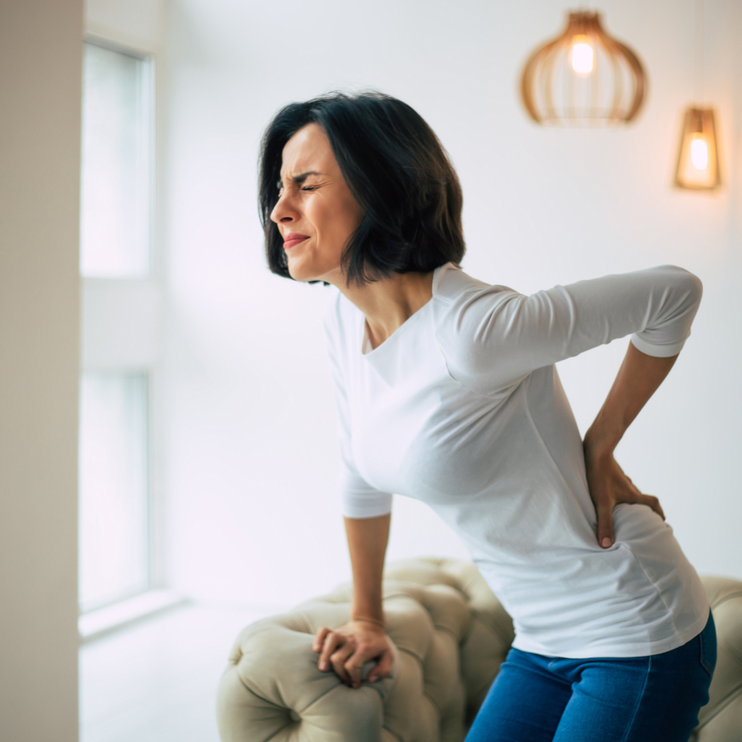 Woman grimacing in pain while holding her lower back, illustrating the need for upper cervical care to alleviate chronic back pain and improve mobility.